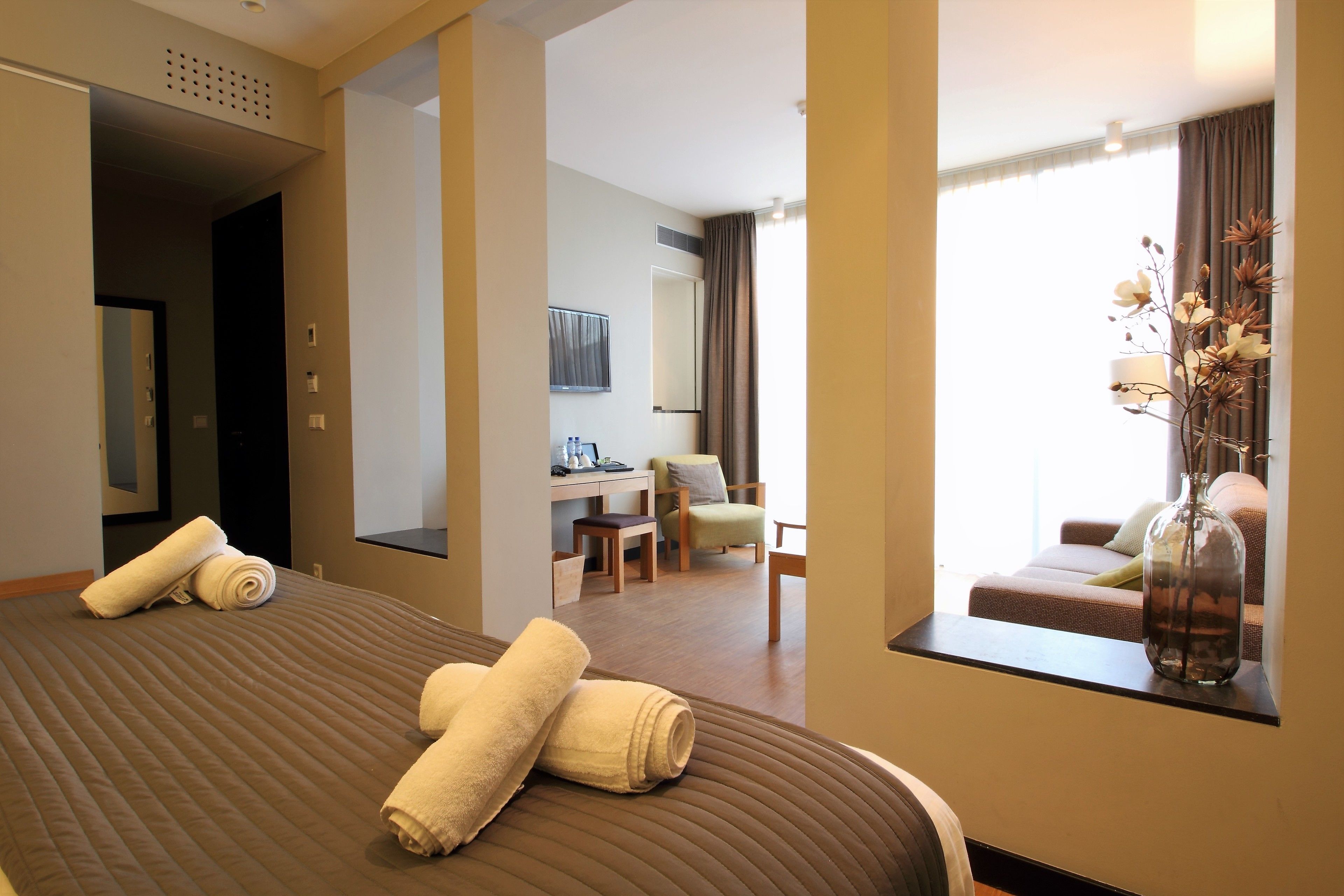 Une chambre d’hôtel avec un lit, un bureau, une chaise, un canapé et un vase rempli de fleurs.