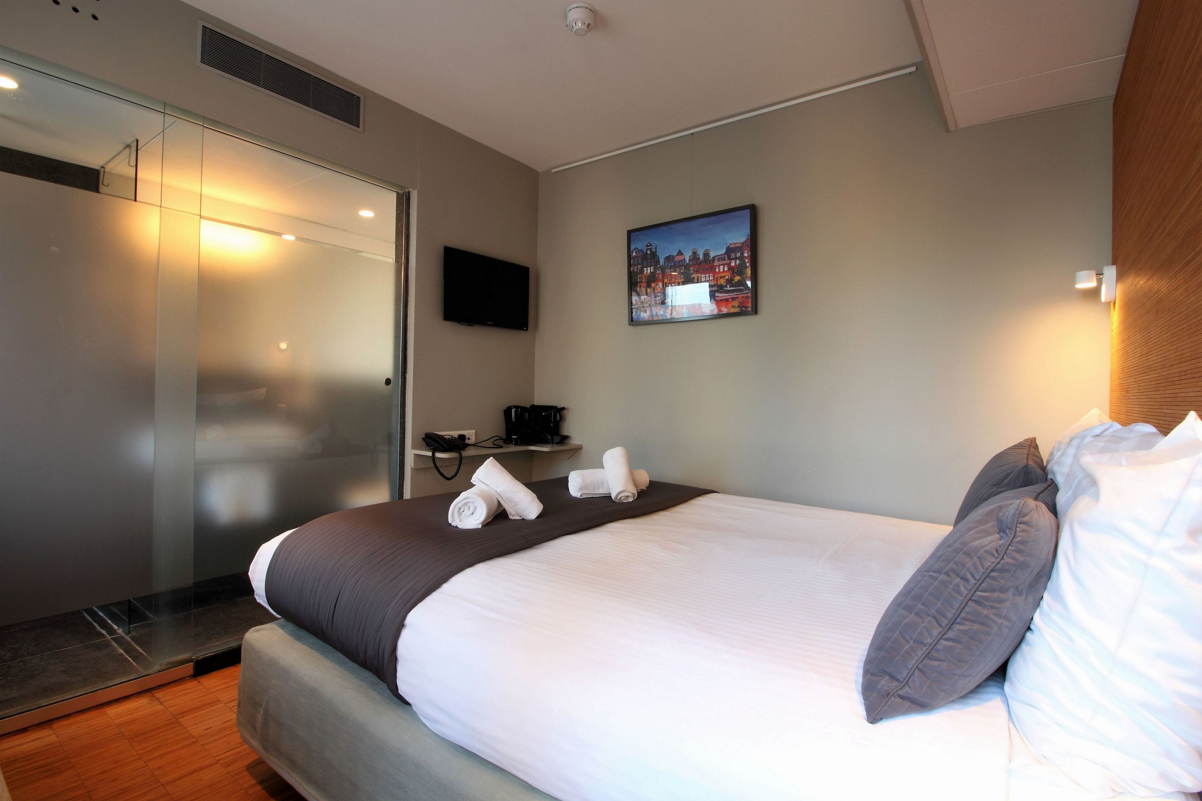 A hotel room with a large bed, a flat-screen TV, a painting on the wall, and a wooden headboard.