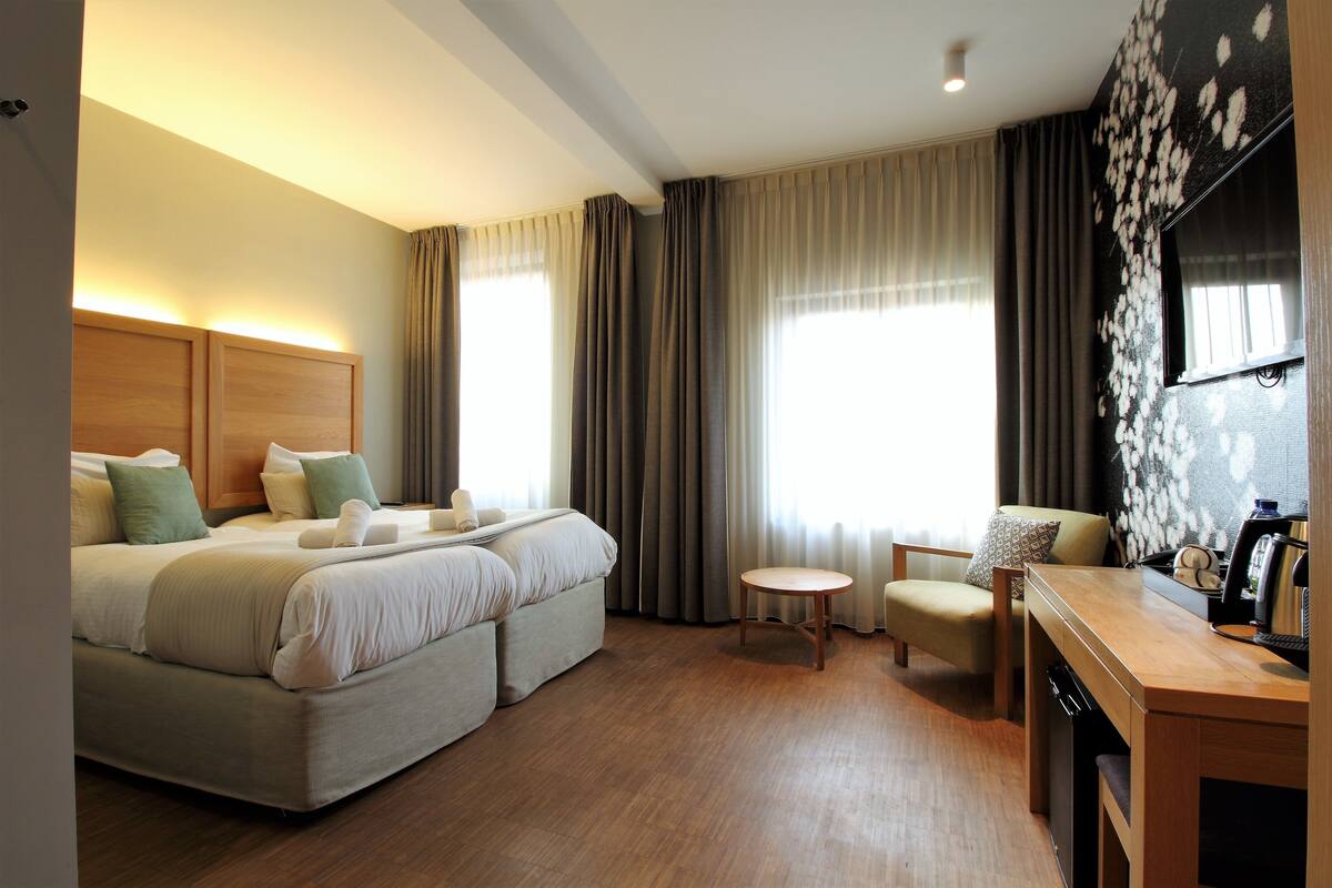 A hotel room with a bed, a desk, a chair, and a large window with curtains.