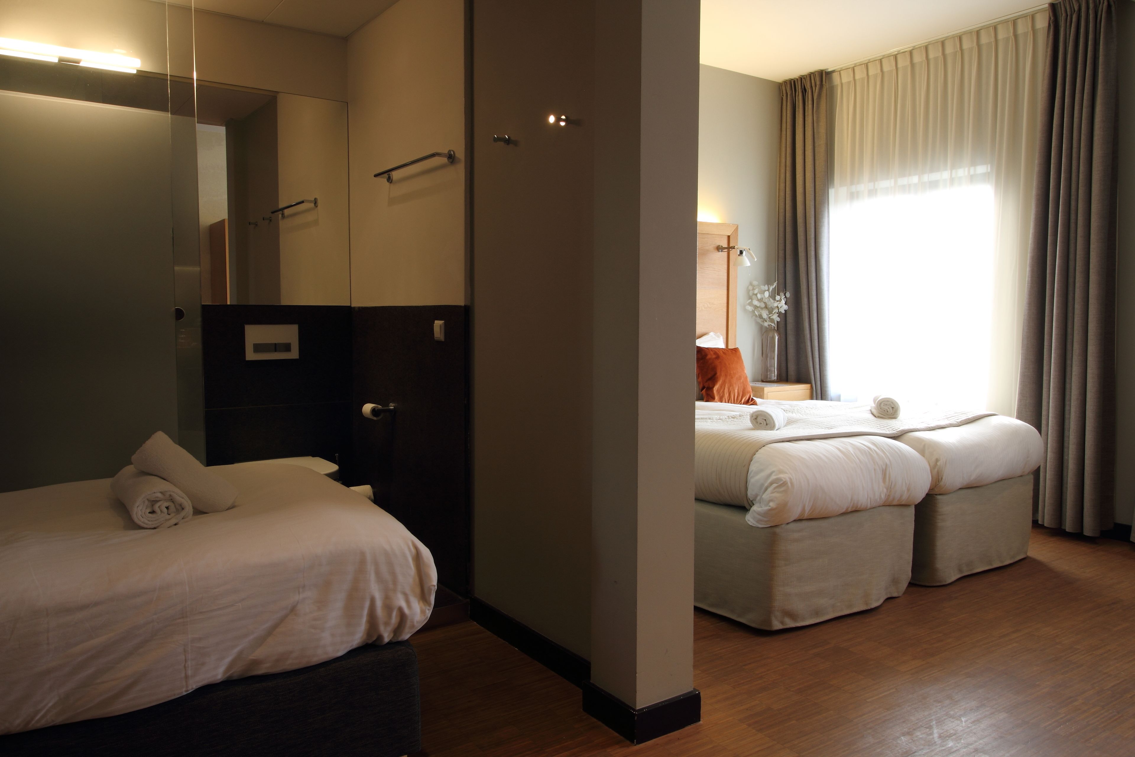 A hotel room with a large bed, a smaller bed, a mirror, a wardrobe, and a window with curtains.