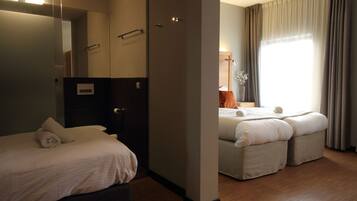 A hotel room with a large bed, a smaller bed, a mirror, a wardrobe, and a window with curtains.