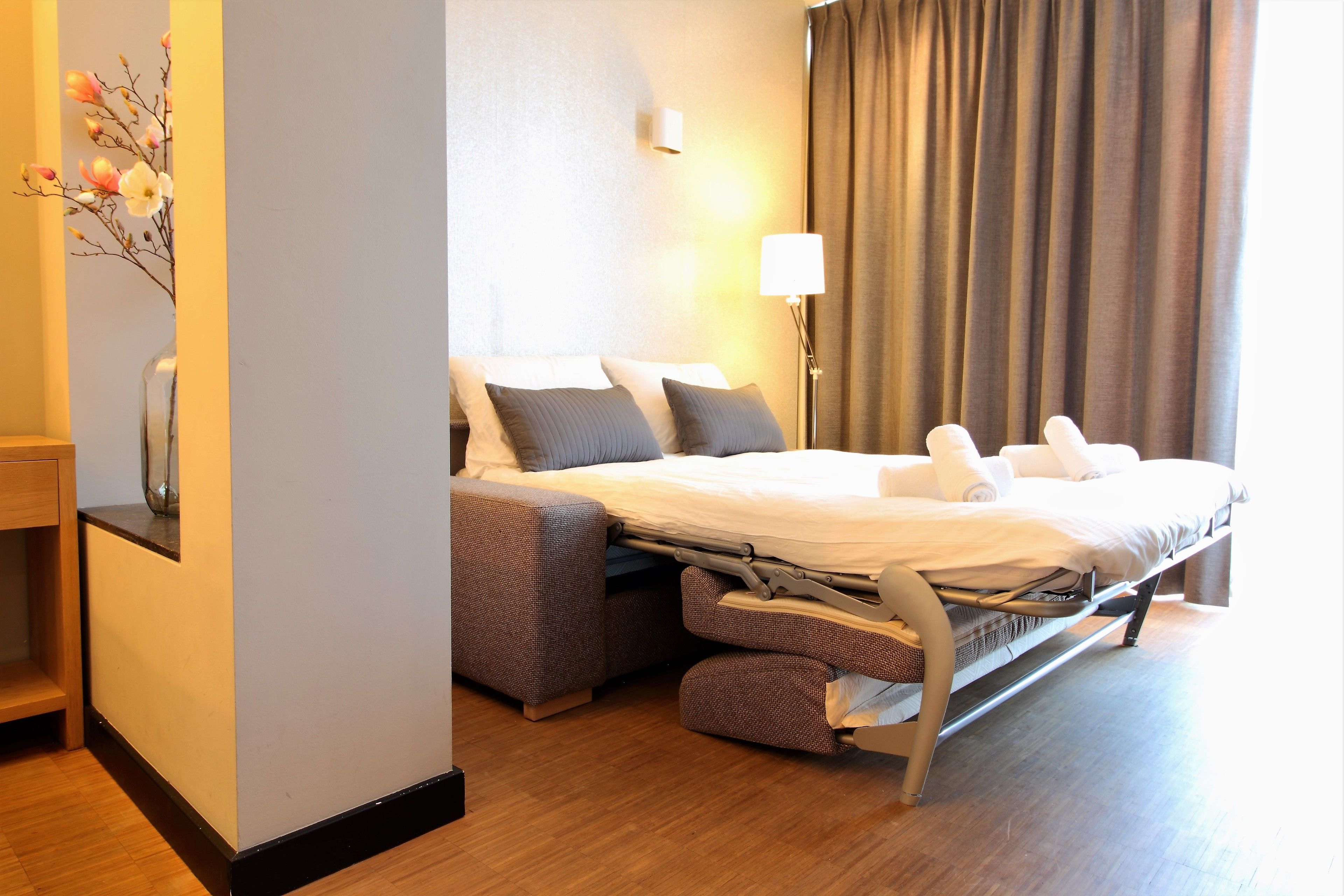 A hotel room with a bed, bedside lamp, and a vase with flowers.