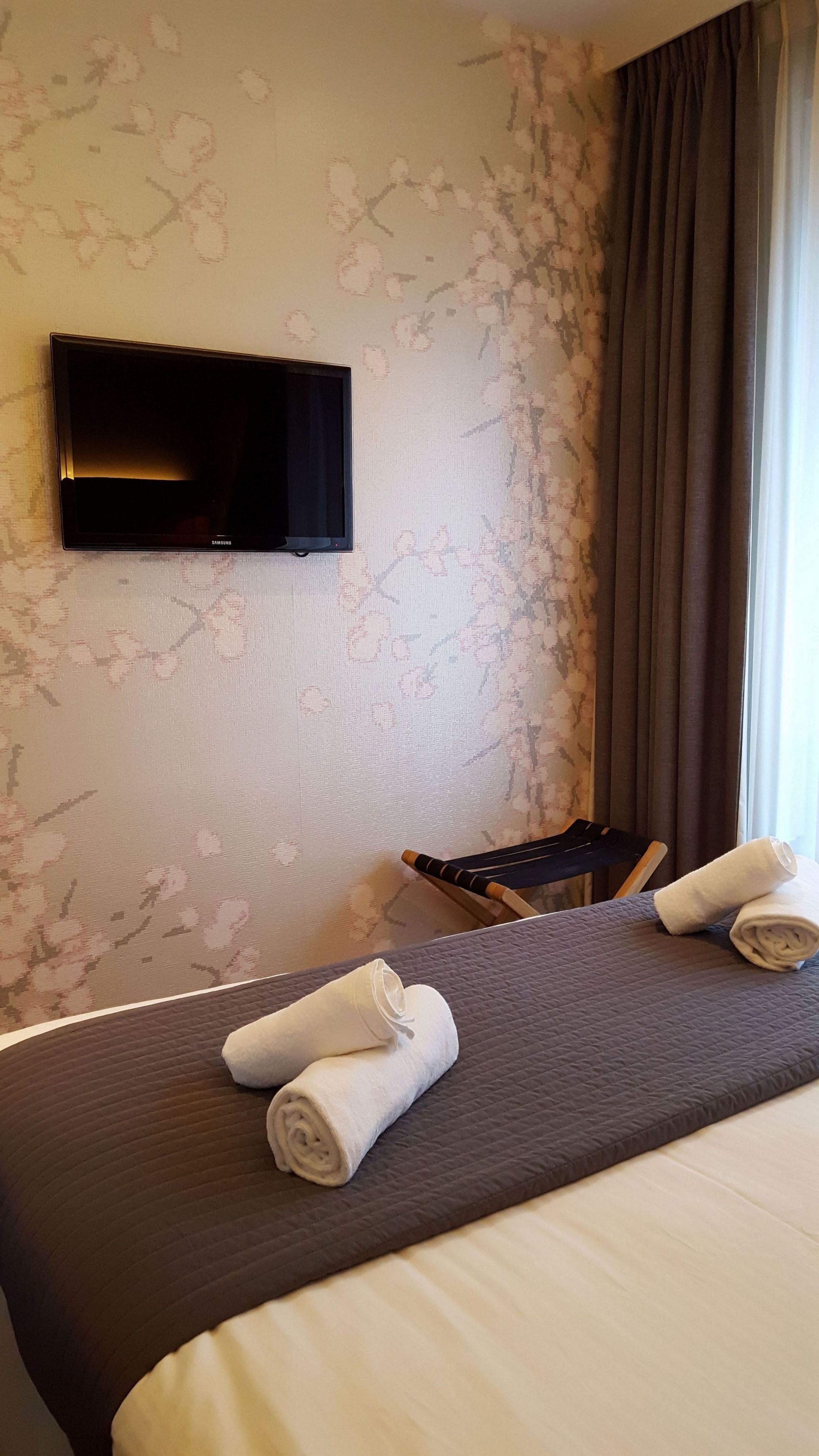 Une chambre d’hôtel avec un lit, un téléviseur à écran plat fixé au mur et une fenêtre avec des rideaux.