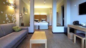 Een moderne hotelkamer met een bank, een klein tafeltje, een bed met houten hoofdbord, een televisie en een koffiezetapparaat.