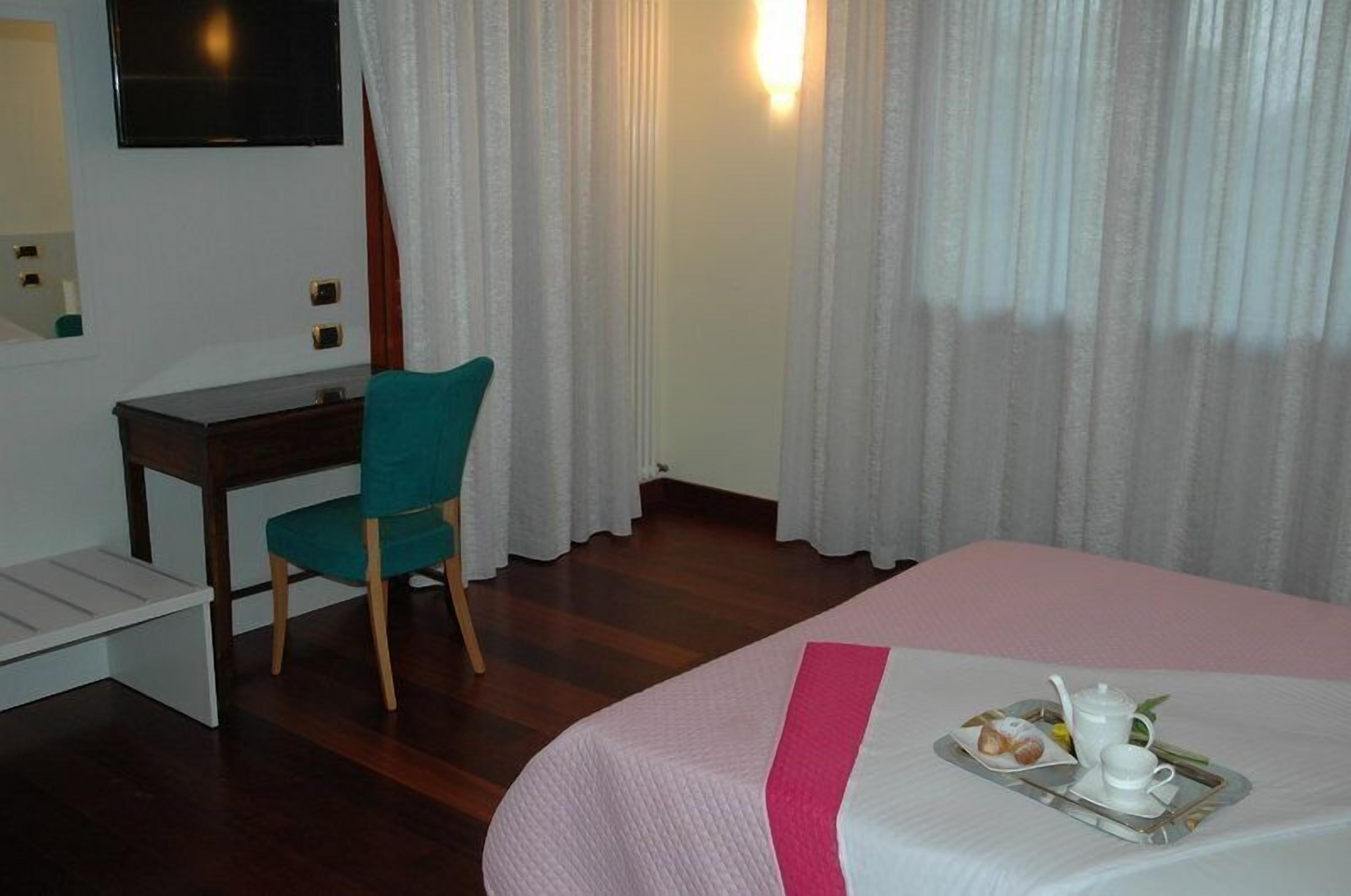 A hotel room with a bed, a desk, a chair, and a tray with breakfast items.