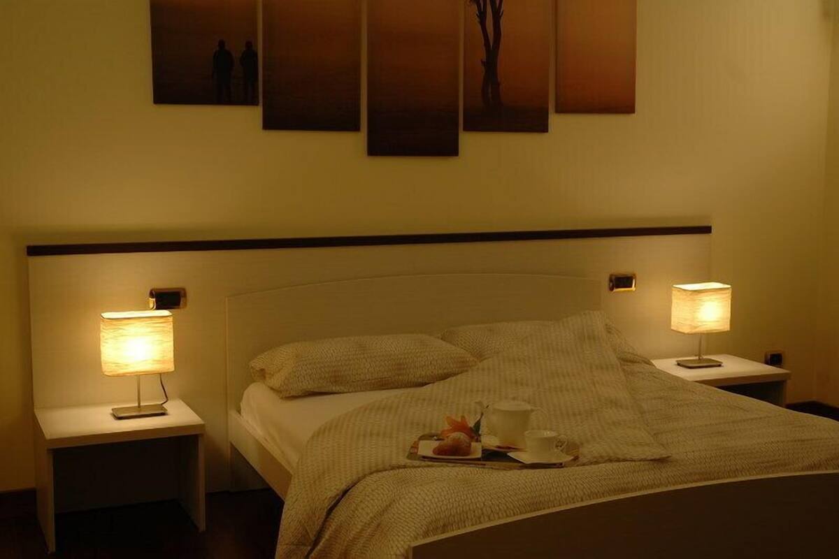 Una cama bien tendida con una bandeja de desayuno, dos lámparas de noche y una obra de arte en la pared.