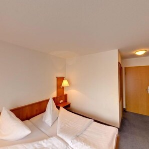 A hotel room with a bed, a nightstand, a lamp, and a door. - Hotel Blume (Freiburg im Breisgau)