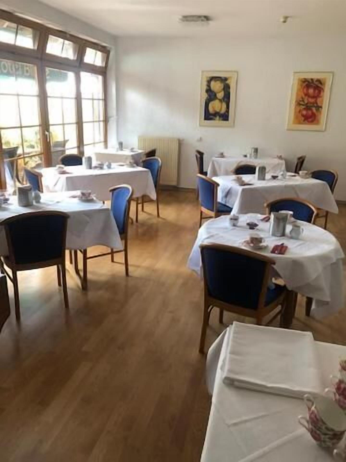Un comedor con mesas y sillas, ventanas amplias y obras de arte en las paredes.
