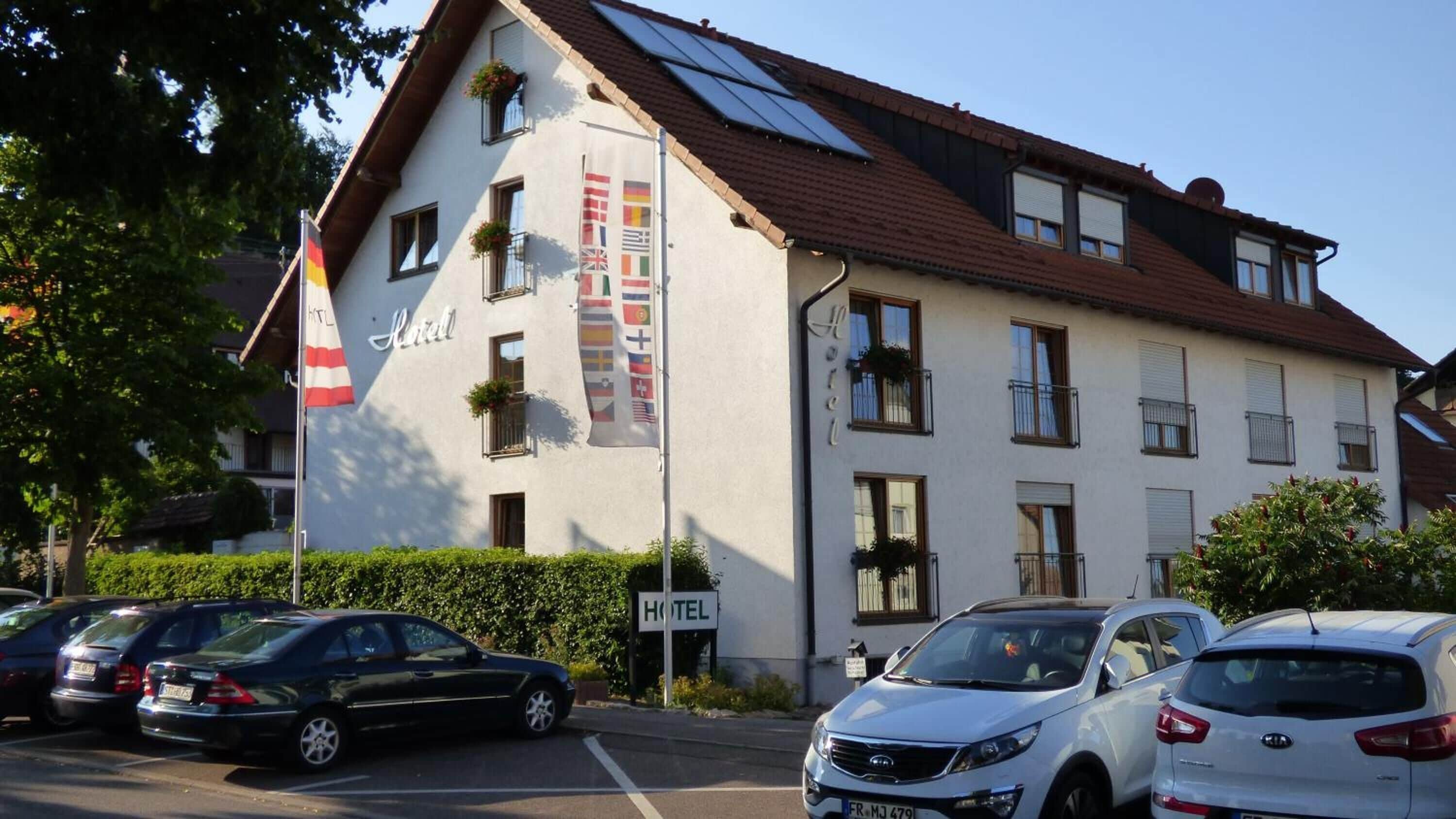Een hotel met meerdere verdiepingen, balkons met beplanting en een wimpelstok met verschillende vlaggen.