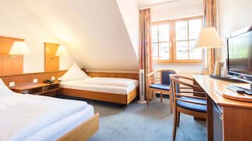 Una habitación de hotel con cama, escritorio, silla, televisor y ventana con cortinas.