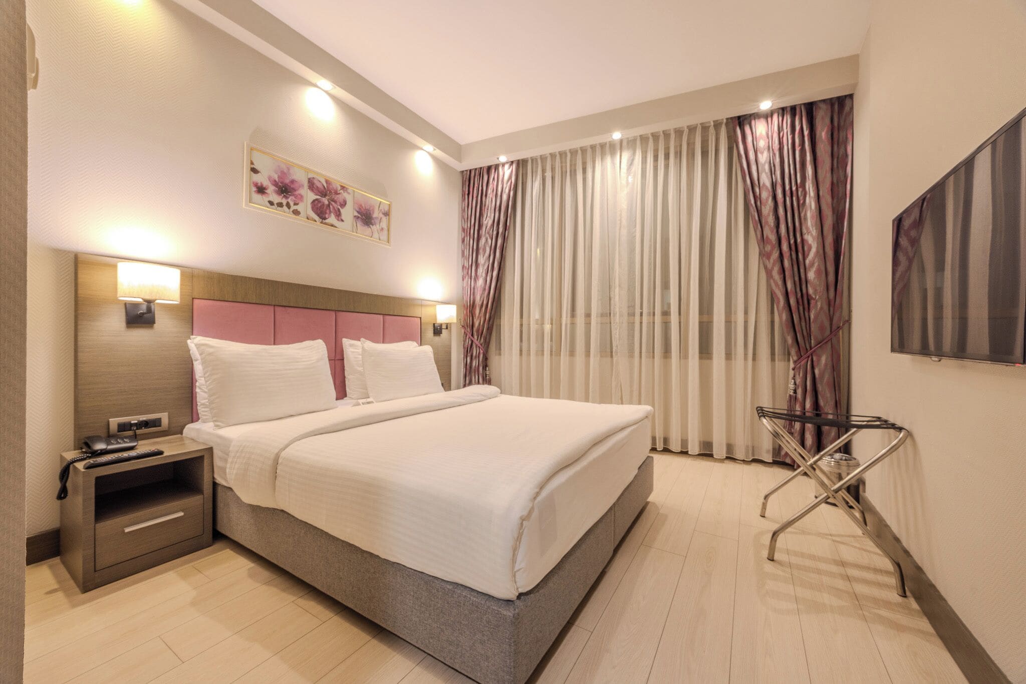 A hotel room with a bed, bedside table, lamp, and a painting on the wall.
