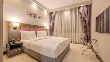 A hotel room with a bed, bedside table, lamp, and a painting on the wall.