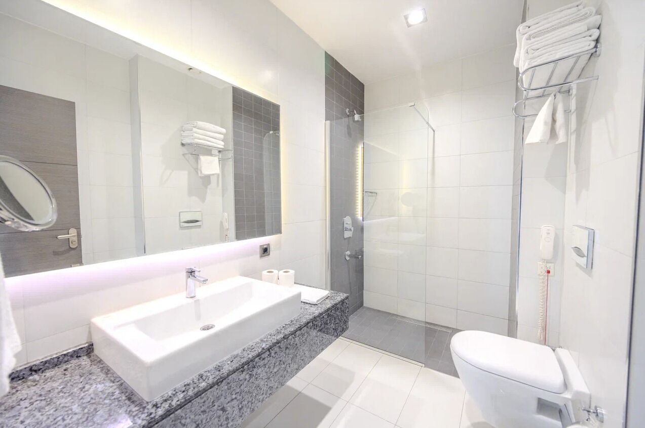 Un baño moderno con un espejo grande, un lavamanos, un inodoro y una ducha con mampara de vidrio.