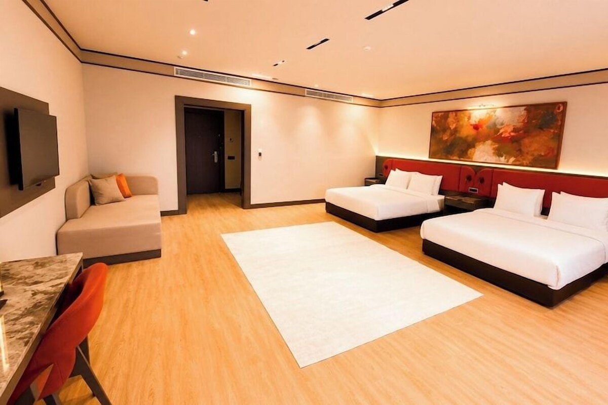 A modern hotel room with two beds, a sofa, a TV, and a large painting on the wall.