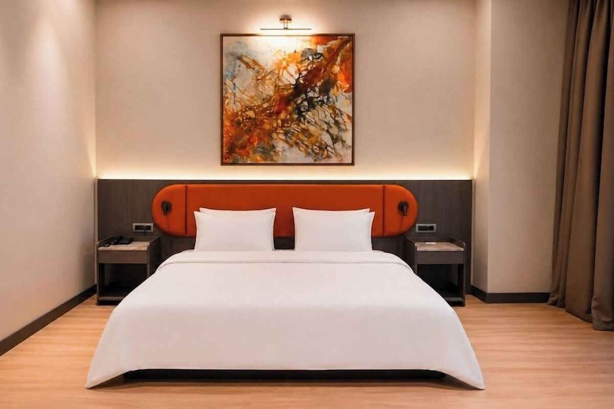 Una camera d'albergo moderna con un letto grande, una testiera di forma circolare, un comodino con una lampada e un'opera d'arte appesa al muro.
