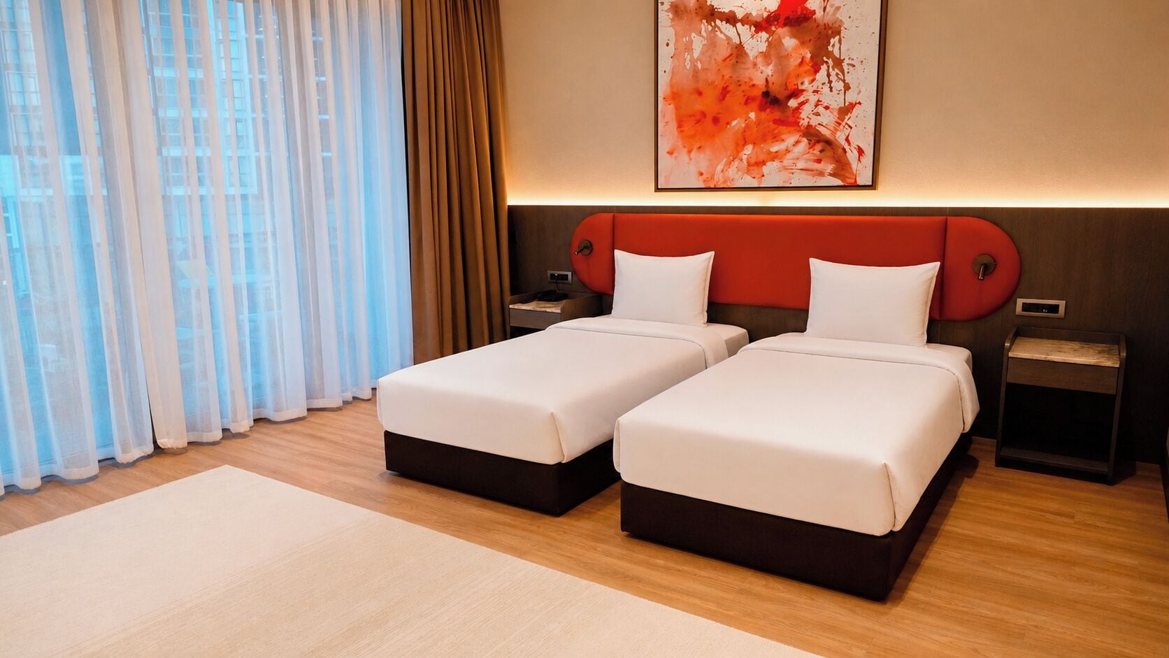 A hotel room with two beds, a large window with sheer curtains, a modern abstract painting, and a wooden floor.