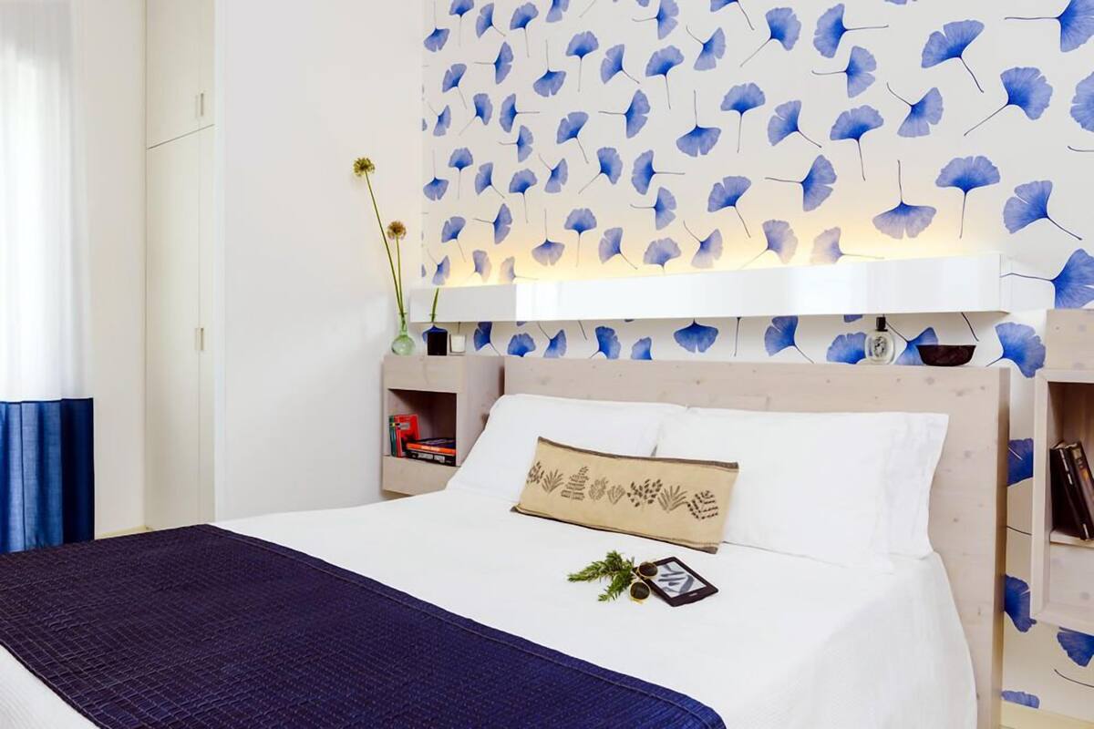 A neatly made bed with a dark blue blanket, a decorative pillow, and a small plant on the bedside table.