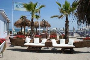 A beachside lounge area with wooden loungers, palm trees, and a view of the sea. - Hotel Torremaura Sea Front (Cervia)