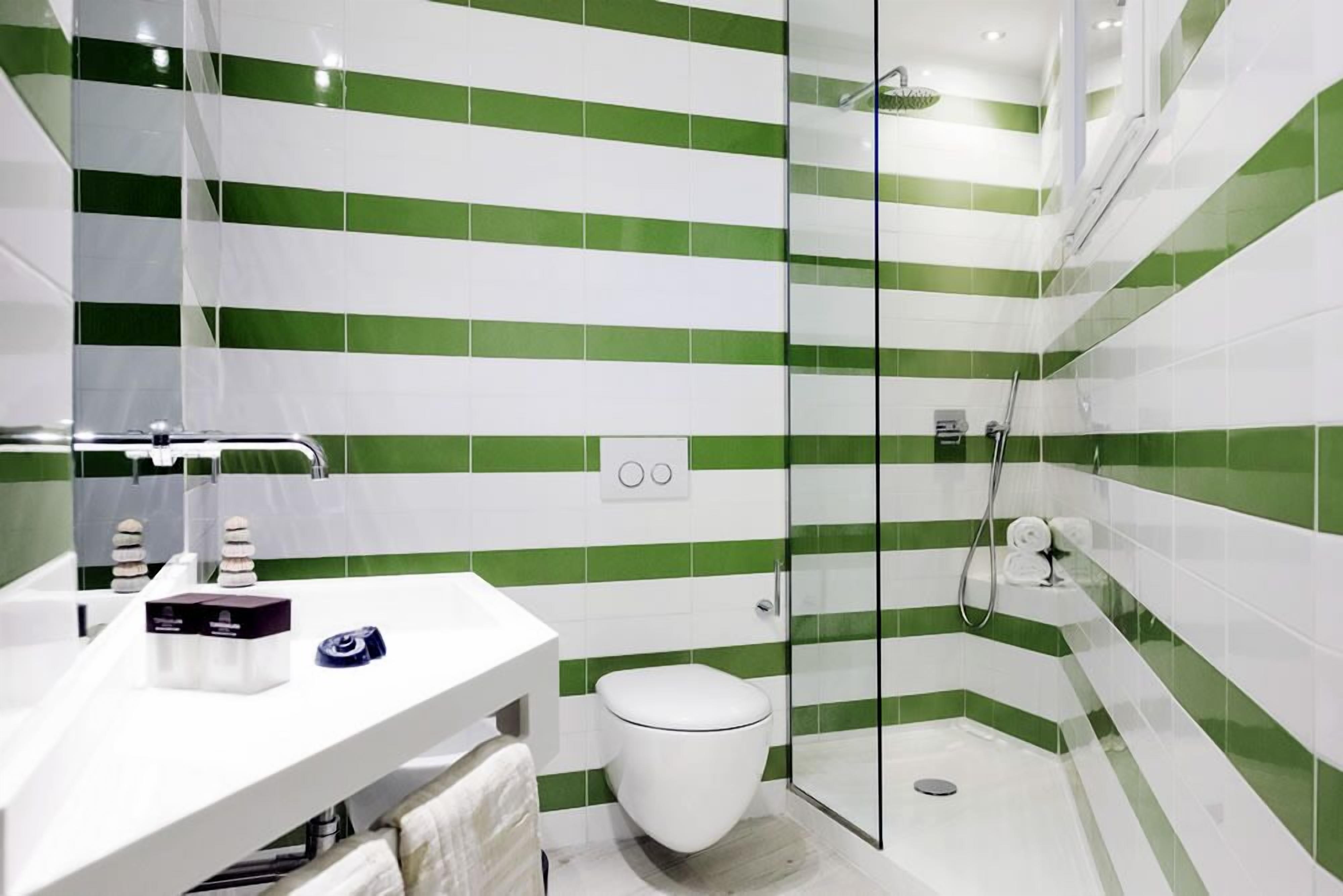 Casa de banho moderna com lavatório branco, sanita e zona de duche com divisória de vidro.