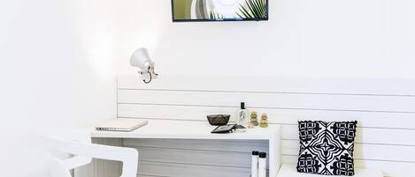 A modern, minimalist room with a white desk, a white chair, a wall-mounted TV, and a decorative pillow.
