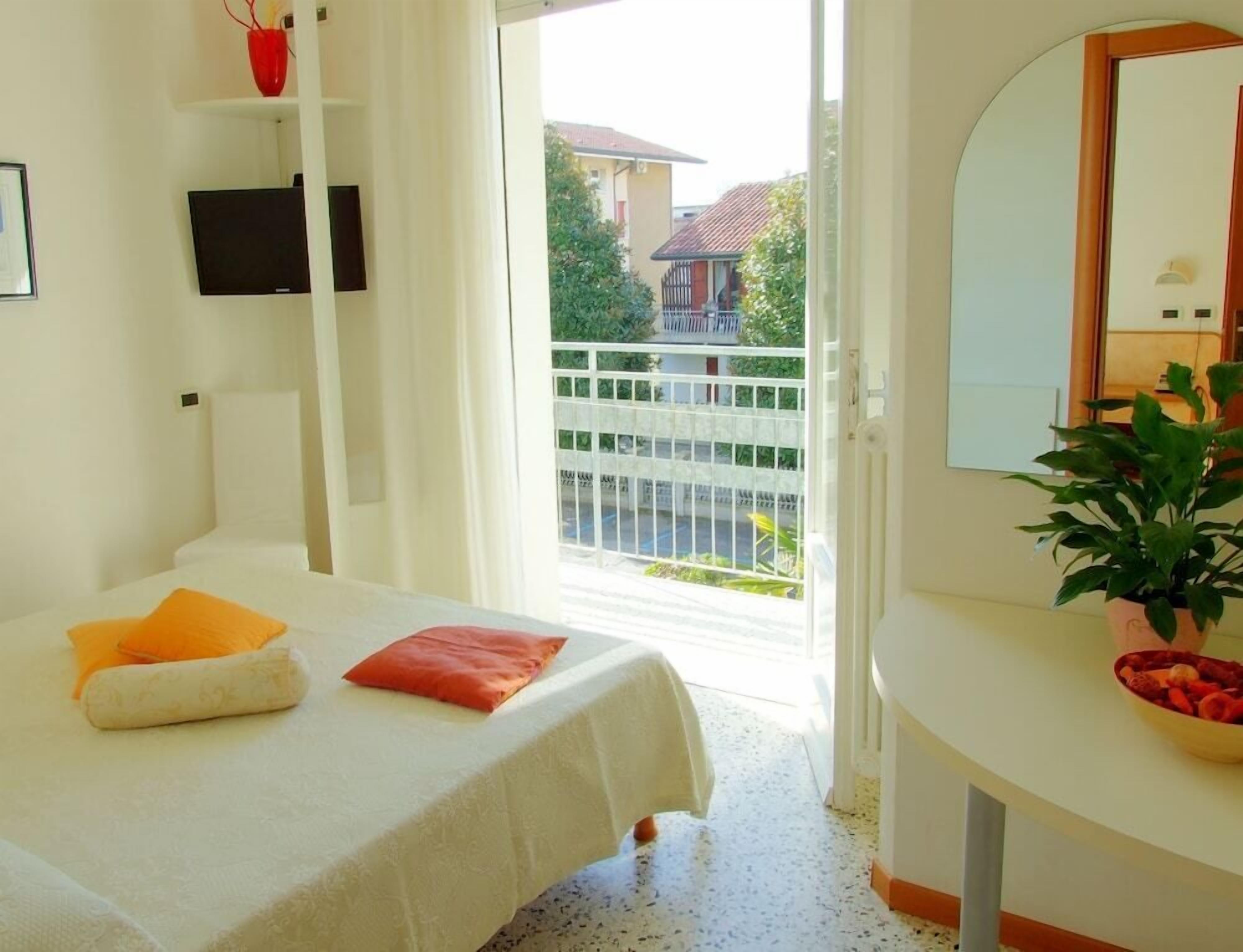 Un dormitorio con cama, mesita de noche, espejo y vistas al exterior.