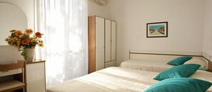 A bedroom with a bed, a nightstand, a wardrobe, a painting on the wall, and a window with curtains.