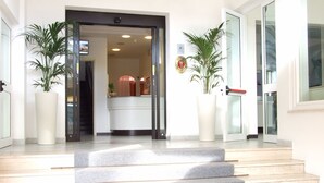 Fachada de un hotel con una escalera que conduce a la recepción. Hay dos plantas grandes a cada lado de la entrada.