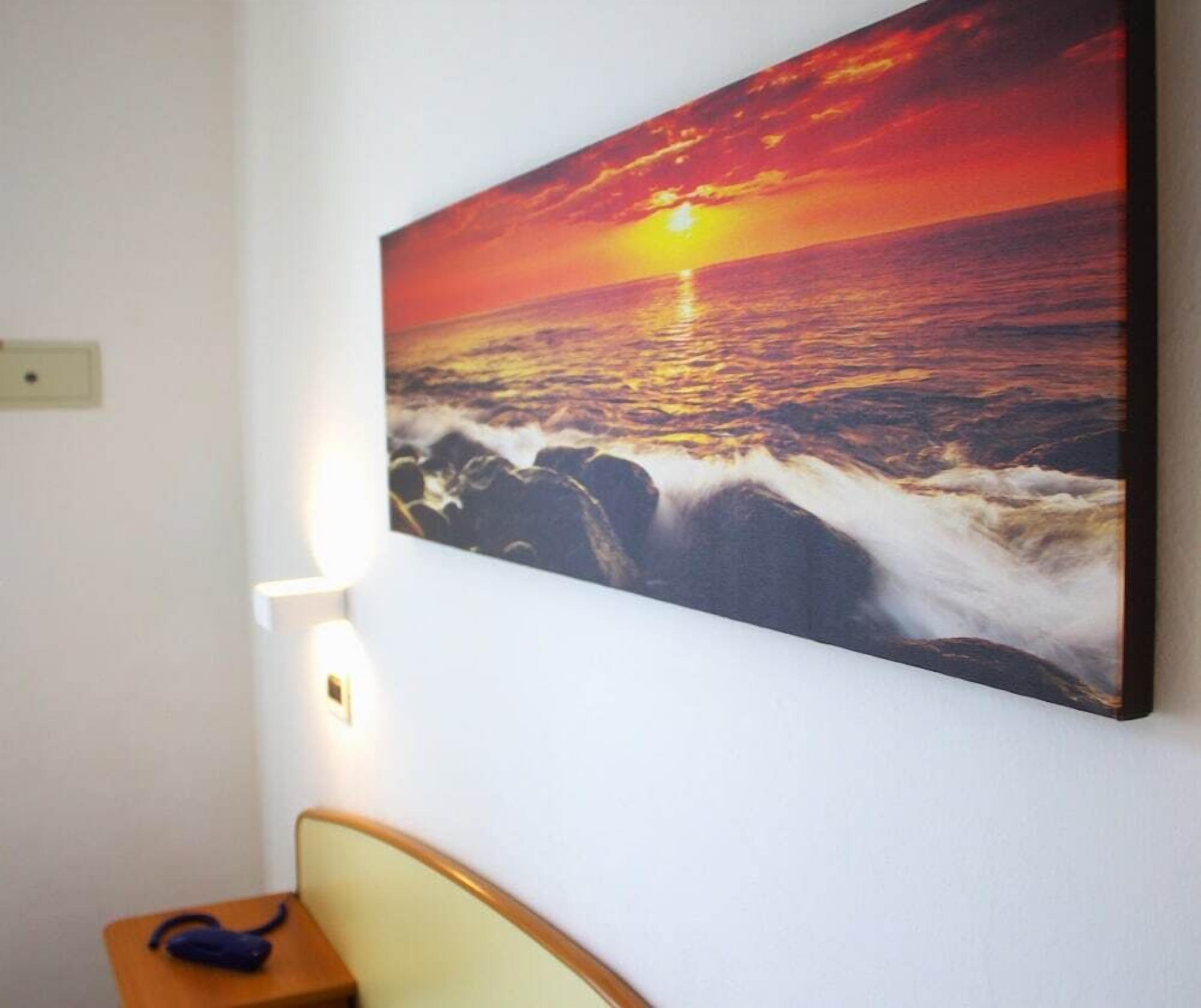 A wall-mounted painting of a sunset over the ocean.
