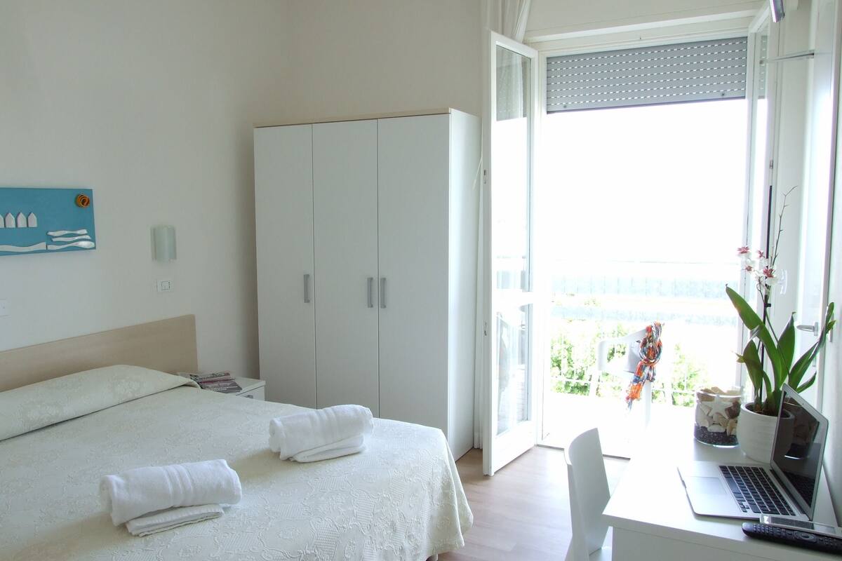 Habitación de hotel con cama, escritorio, laptop, silla y armario.