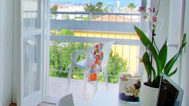 Un balcón con vista al mar, una silla, una planta en maceta y un recipiente de vidrio con flores.