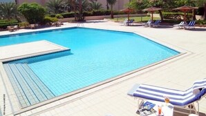 Ein Swimmingpool mit Liegestühlen und Sonnenschirmen, umgeben von Palmen und einem Hotelgebäude der Marriott.
