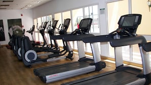 Reihe von Laufbändern in einem Fitnessstudio mit großen Fenstern und Holzboden.