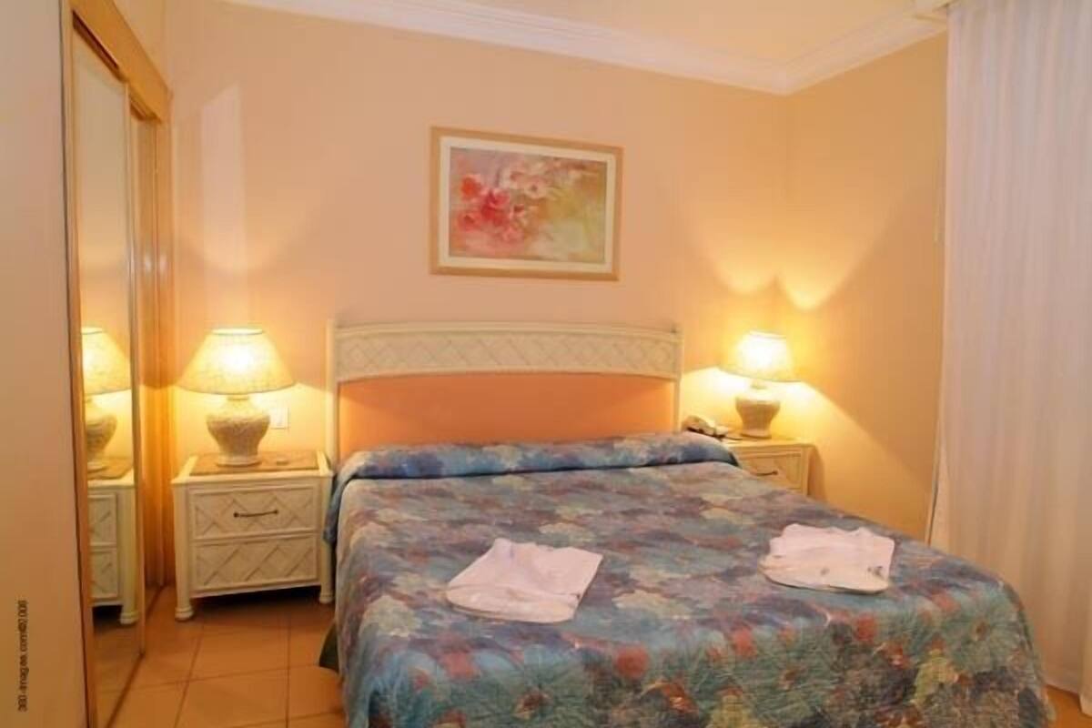 A hotel room with a bed, two bedside lamps, a nightstand, and a painting on the wall.