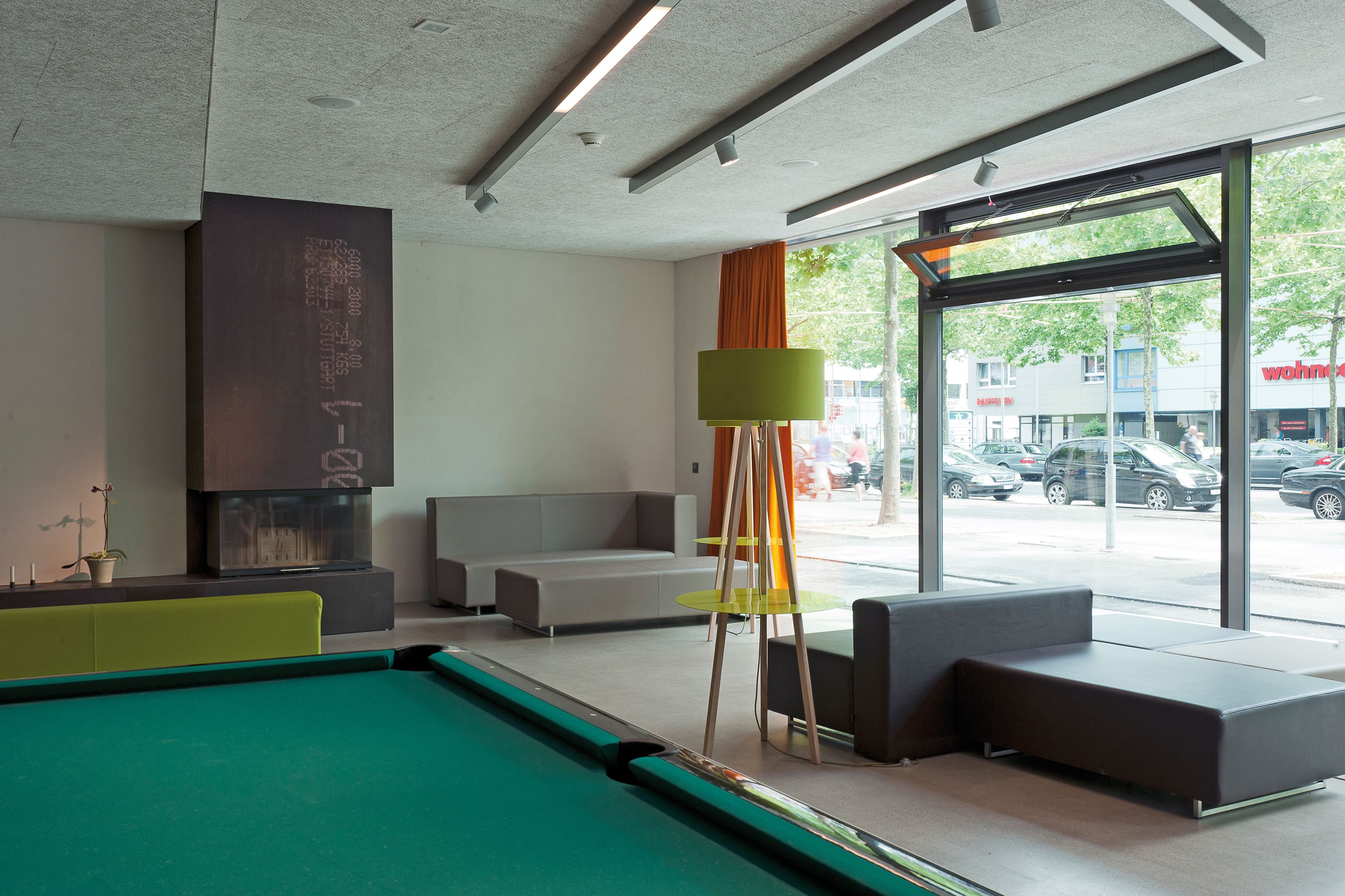 Ein moderner Poolbereich im Innenbereich mit einem grünen Billardtisch, Sitzgelegenheiten und einem großen Fenster mit Blick auf die Straße.
