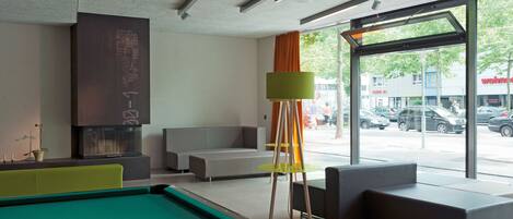 A modern indoor pool area with a green pool table, seating, and a large window offering a view of the street.