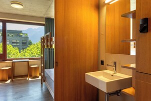 Un baño moderno con tocador de madera, un lavamanos blanco y vistas a las montañas a través del ventanal.