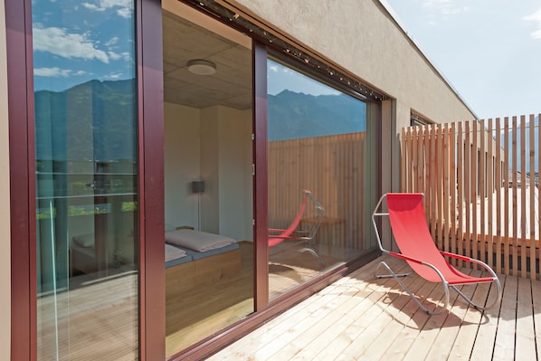 Ein modernes Zimmer mit Glastür zu einem Balkon, einem roten Sessel und einem Bett mit Bergblick.