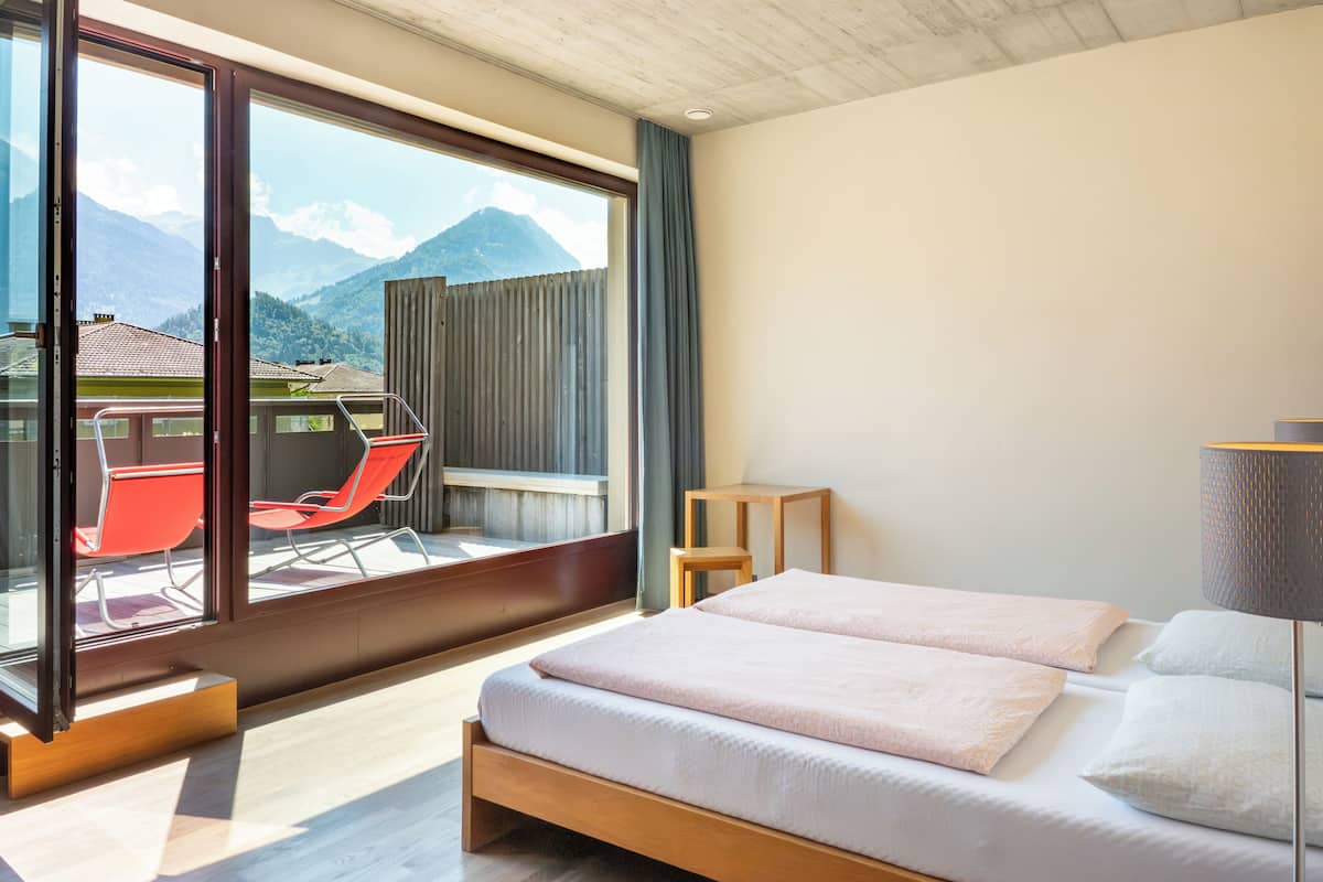 A bedroom with a large window, a bed, a chair, and a small table.