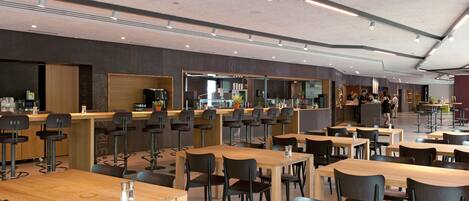 A modern restaurant with multiple tables and chairs, a bar area, and a counter with a coffee machine.