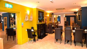 A restaurant with yellow walls, a fireplace, and multiple dining tables and chairs. - Dolphin Rooms (Cleethorpes)