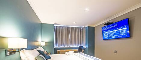 Una habitación de hotel moderna con cama, mesita de noche, lámpara y televisor que muestra información de vuelos.