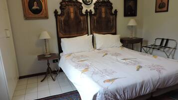 A bedroom with a large bed, two bedside tables, a chair, a rug, and framed pictures on the wall.