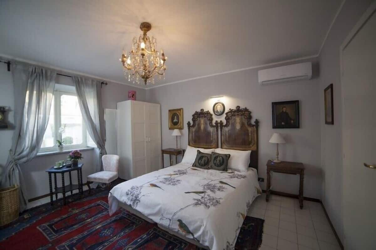 Un dormitorio con una cama grande, una araña, una silla, un armario y una mesita.