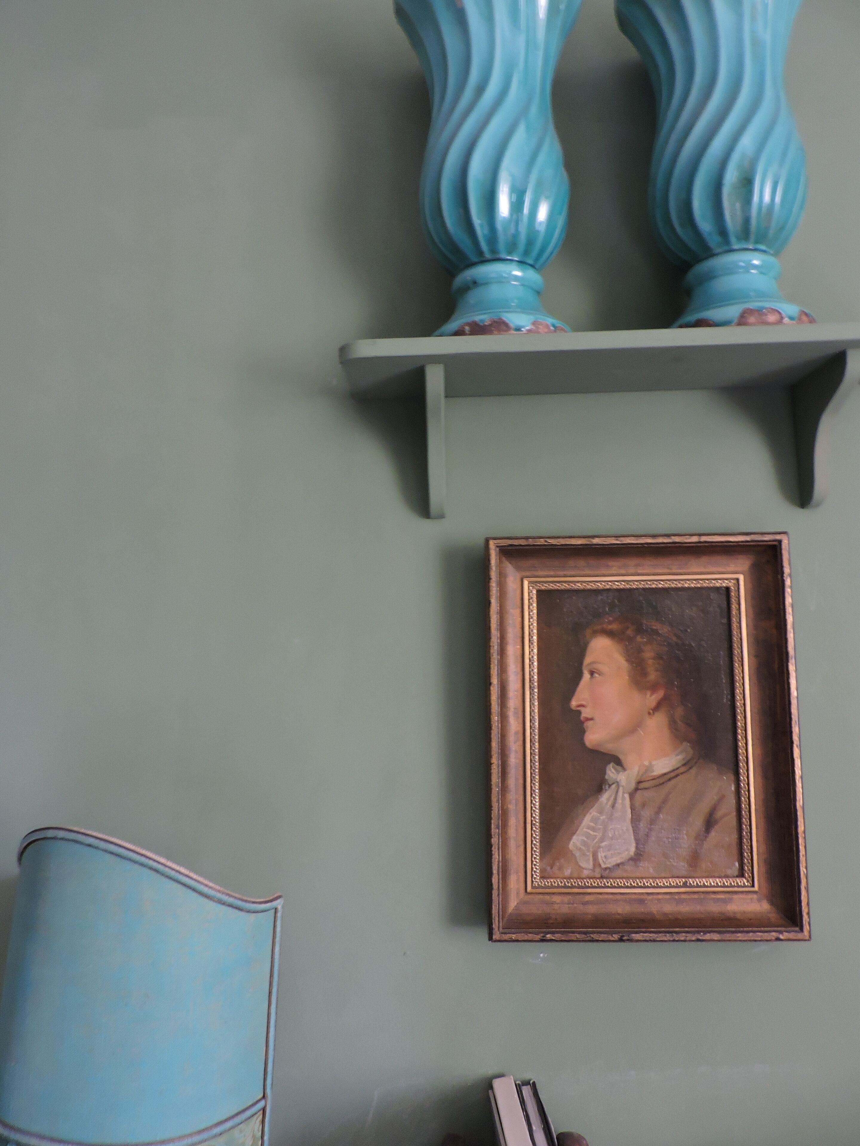 A room with a teal wall, a framed portrait, and a blue chair.