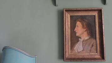 A room with a teal wall, a framed portrait, and a blue chair.