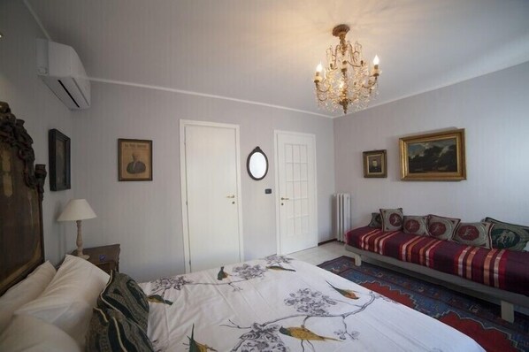 A bedroom with a bed, a sofa, a chandelier, and a door.