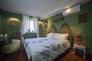 A bedroom with a large bed, a chair, a nightstand, and a window with curtains.