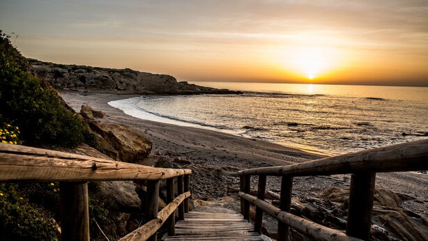 A wooden staircase leading to a beach with a sunset in the background. - Hotel Boutique Milla de Plata (San Roque)