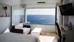 A room with a bed, a sofa, a small table, a TV, and a window with a view of the sea. - Hotel Boutique Milla de Plata (San Roque)