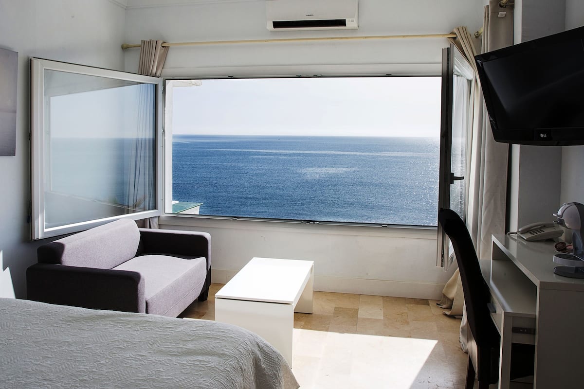 Una habitación con cama, sofá, una mesita, televisor y ventana con vista al mar.